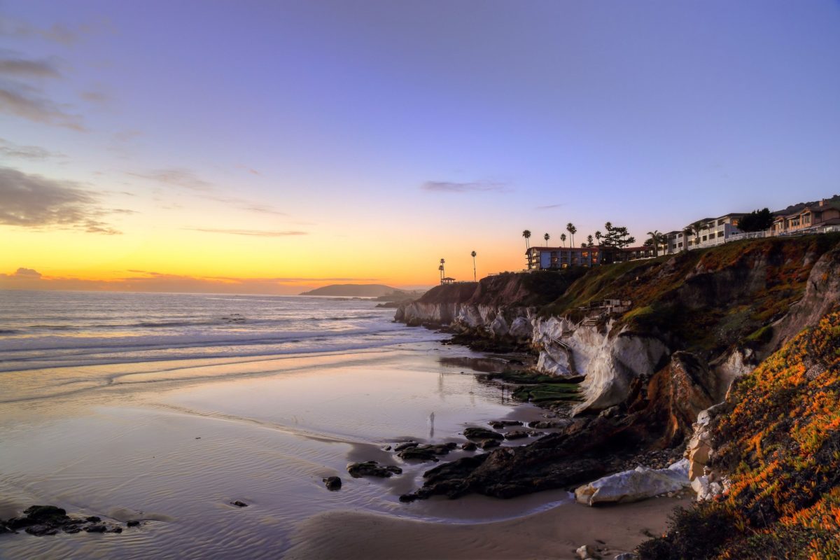 A view of condo buildings on a cliff above the ocean. at sunset